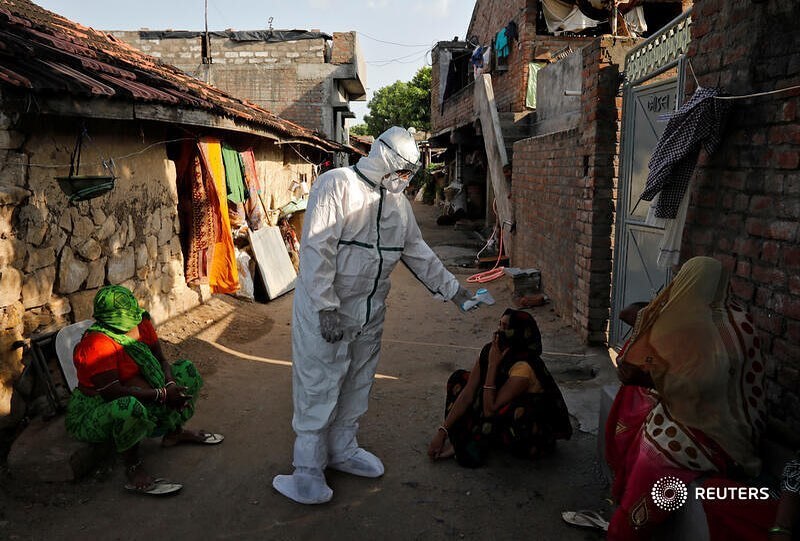 A healthcare worker wearing personal protective equipment (PPE) checks the temperature of a woman sitting outside her house in an alley during a door-to-door survey for the coronavirus disease (COVID-19), in Jakhan village in the western state of Gujarat, India, September 22, 2020. REUTERS/Amit Dave
