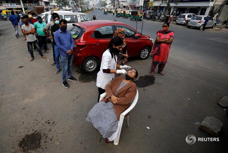 A healthcare worker collects a swab sample from a woman as others wait for their turn during a rapid antigen testing drive for the coronavirus disease (COVID-19) at a roadside in Ahmedabad, India, January 5, 2022. REUTERS/Amit Dave